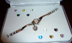 Never worn ladies silver band watch is brand new in box. It has a heart locket attached (or can be removed) with 10 interchangeable heart stones in several different colours of your choice. Was gift for our daughter but she doesn't wear watches so it was