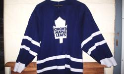 TML, white on blue (away game or practice) jersey.
CCM brand, mens size medium.
White Maple Leafs patch on front.
One leaf (old logo) patch on each sleeve.
No name, no number.